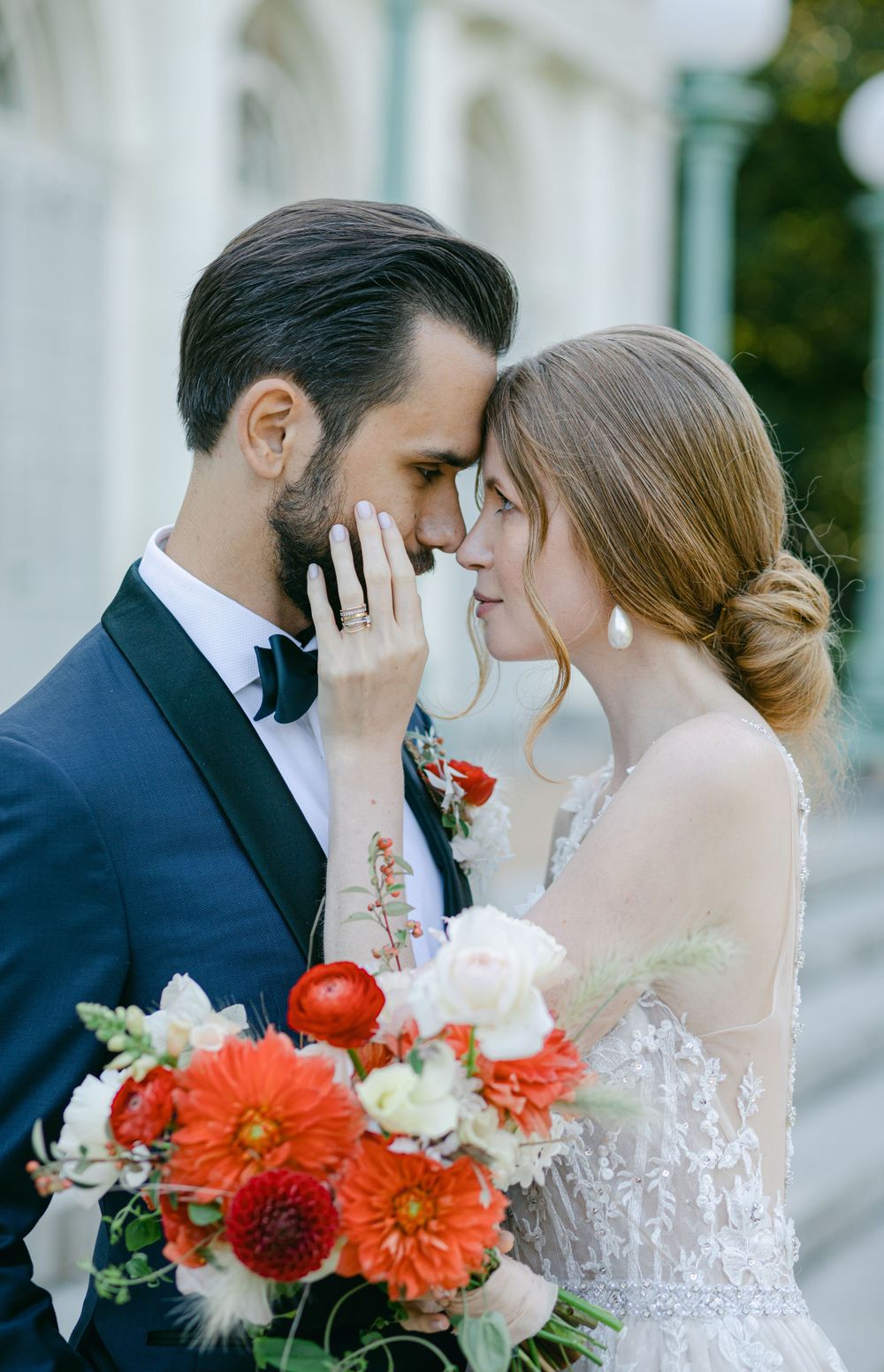 An intimate wedding portrait with bright coral dahlias and roses in front of a white facade.