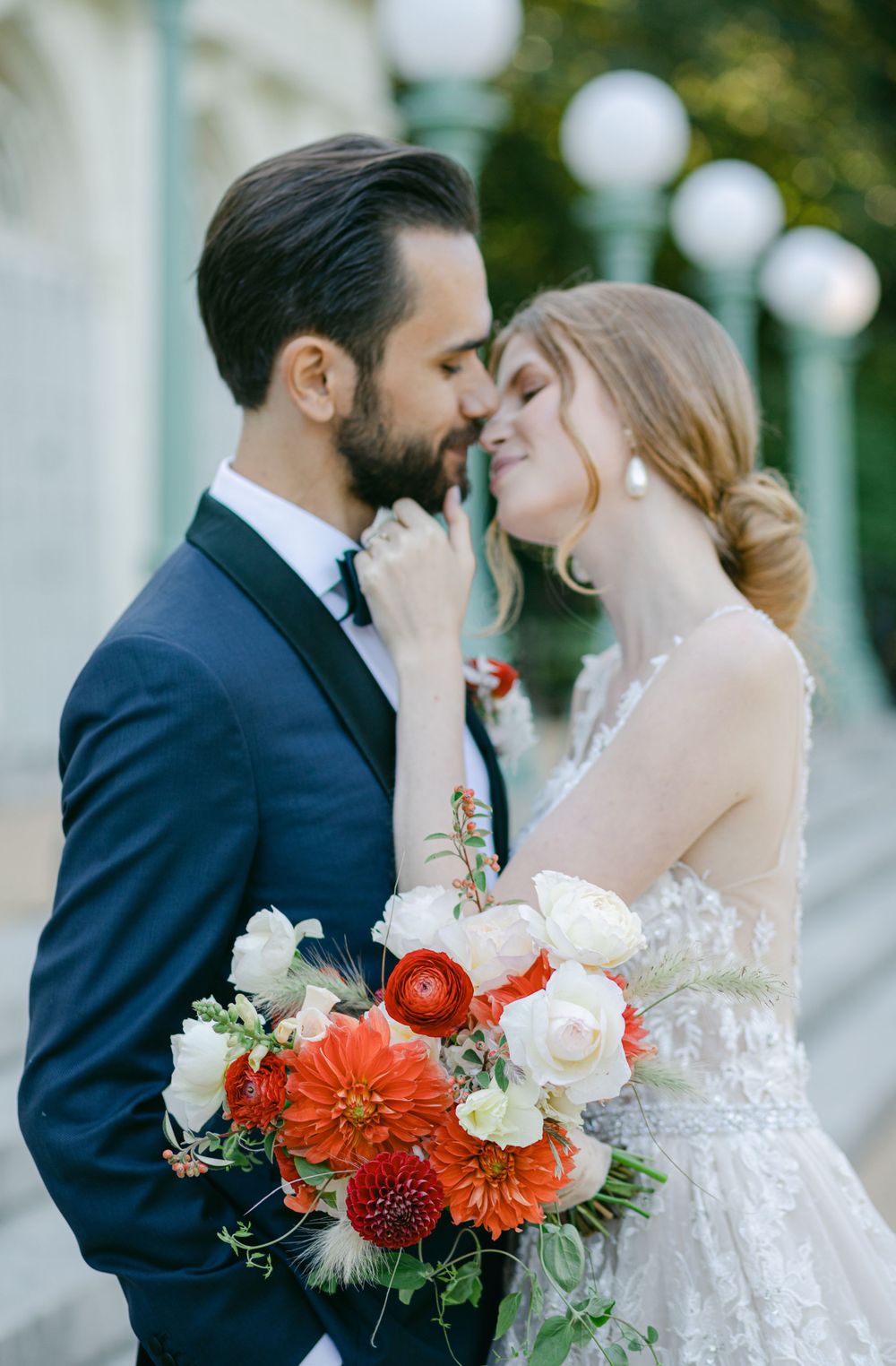 A romantic wedding embrace with coral and white florals against a backdrop of string lights.