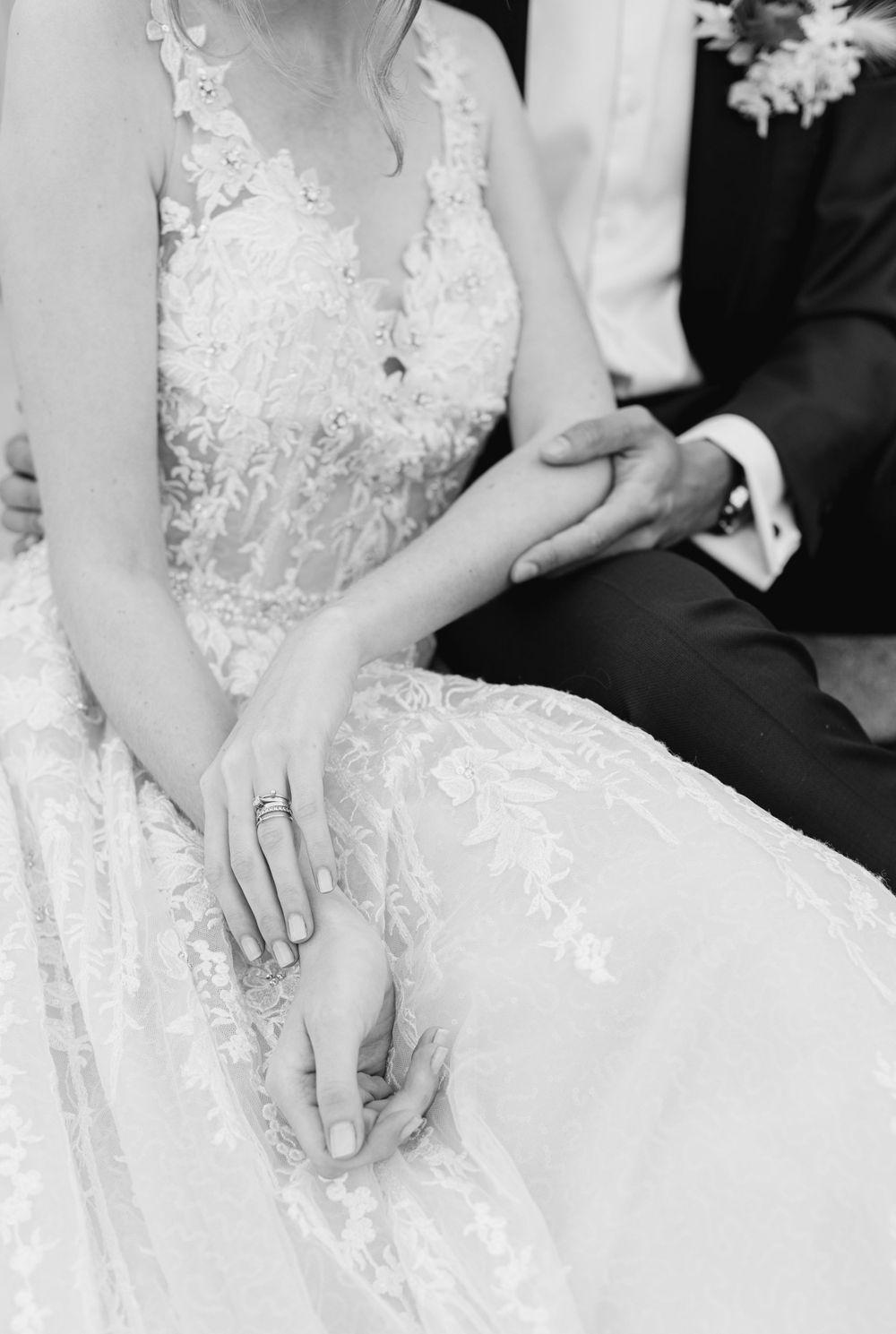 A detail shot of lace wedding dress and hands showing delicate bridal jewelry in black and white.