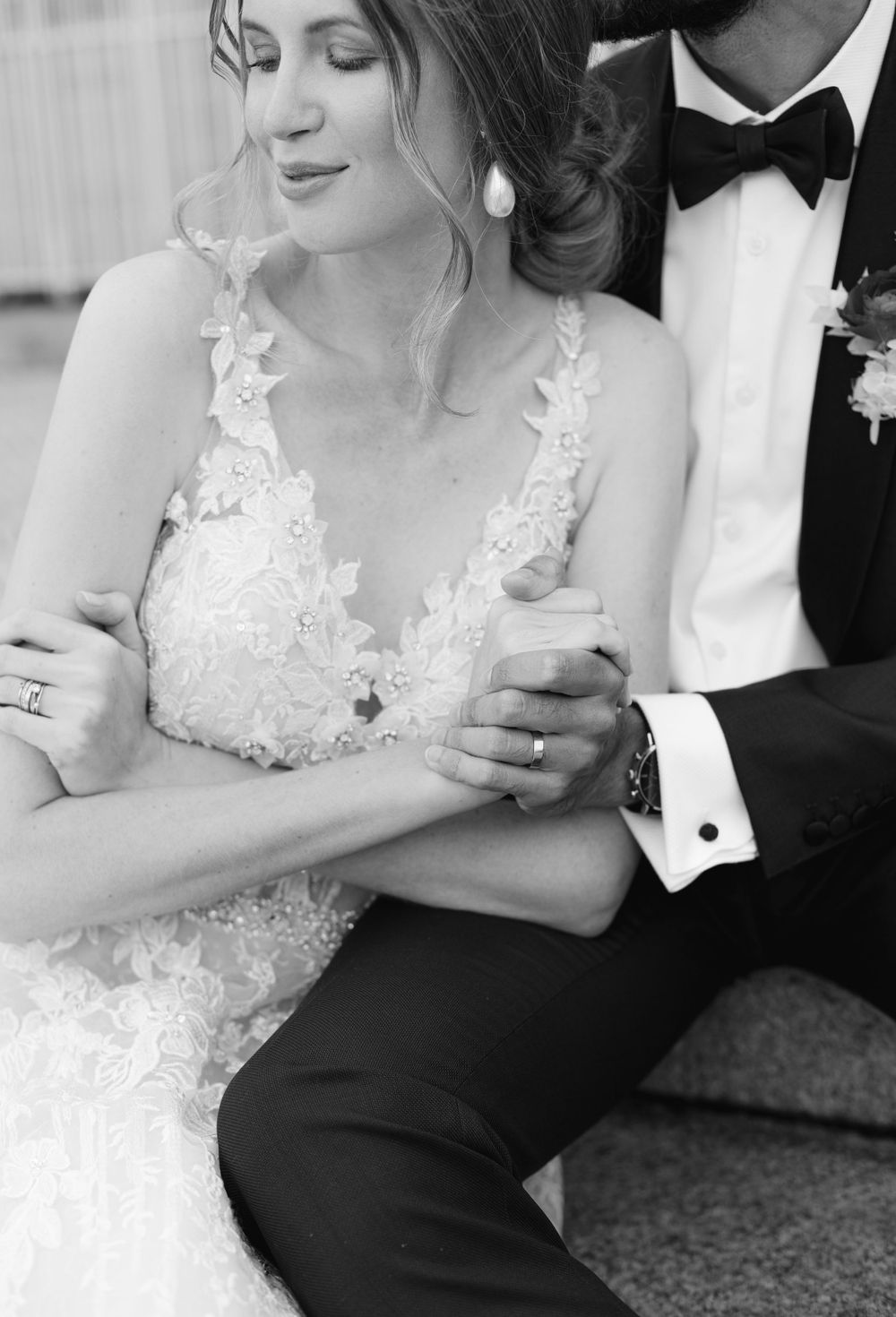 Black and white wedding photo showing delicate lace details on a bride's dress with elegant jewelry accents.
