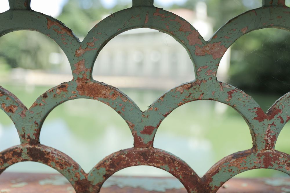 Rustic teal metal gate with scalloped pattern showing weathered patina.