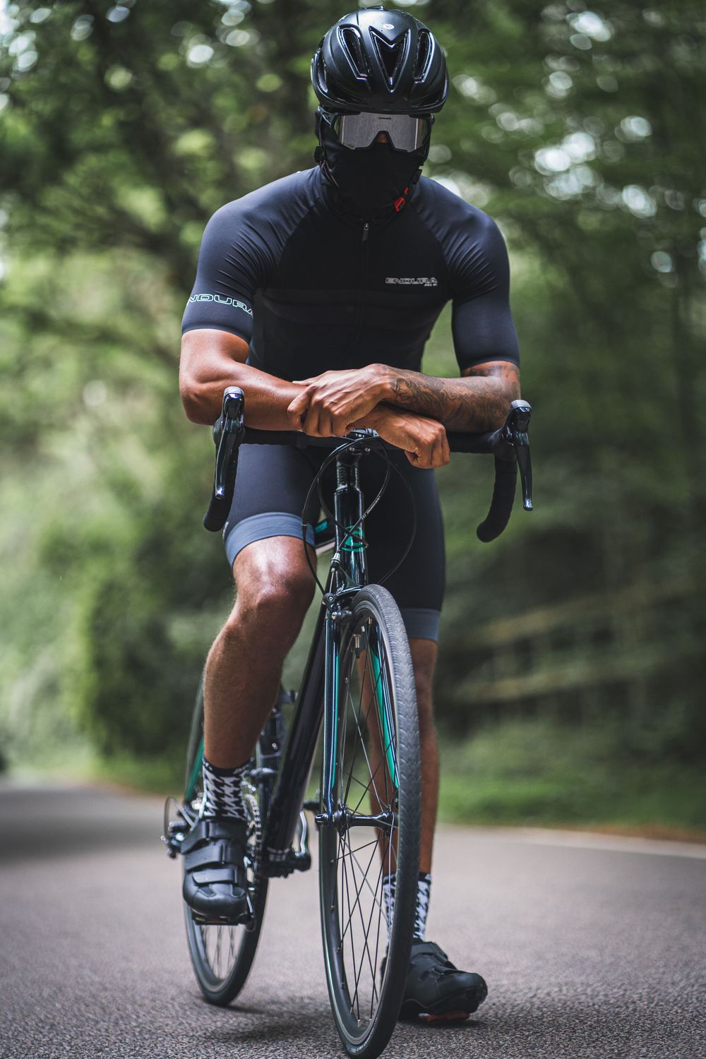 Cyclist in black gear and helmet rides on forest road.