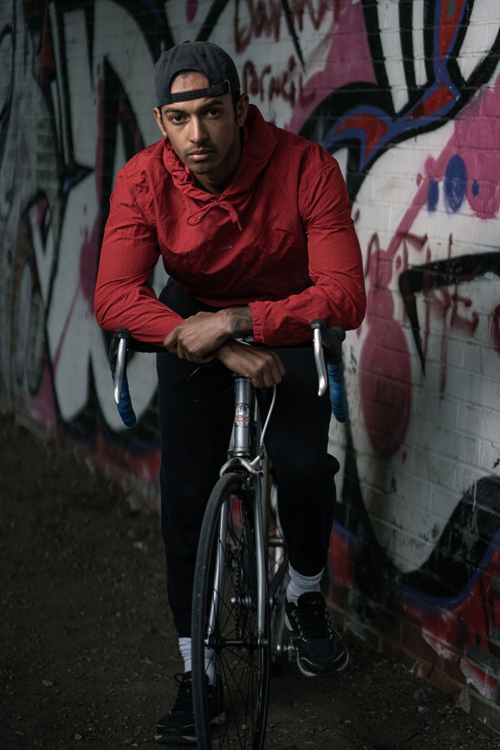 A cyclist in red athletic wear leans on bike handle against urban graffiti wall.