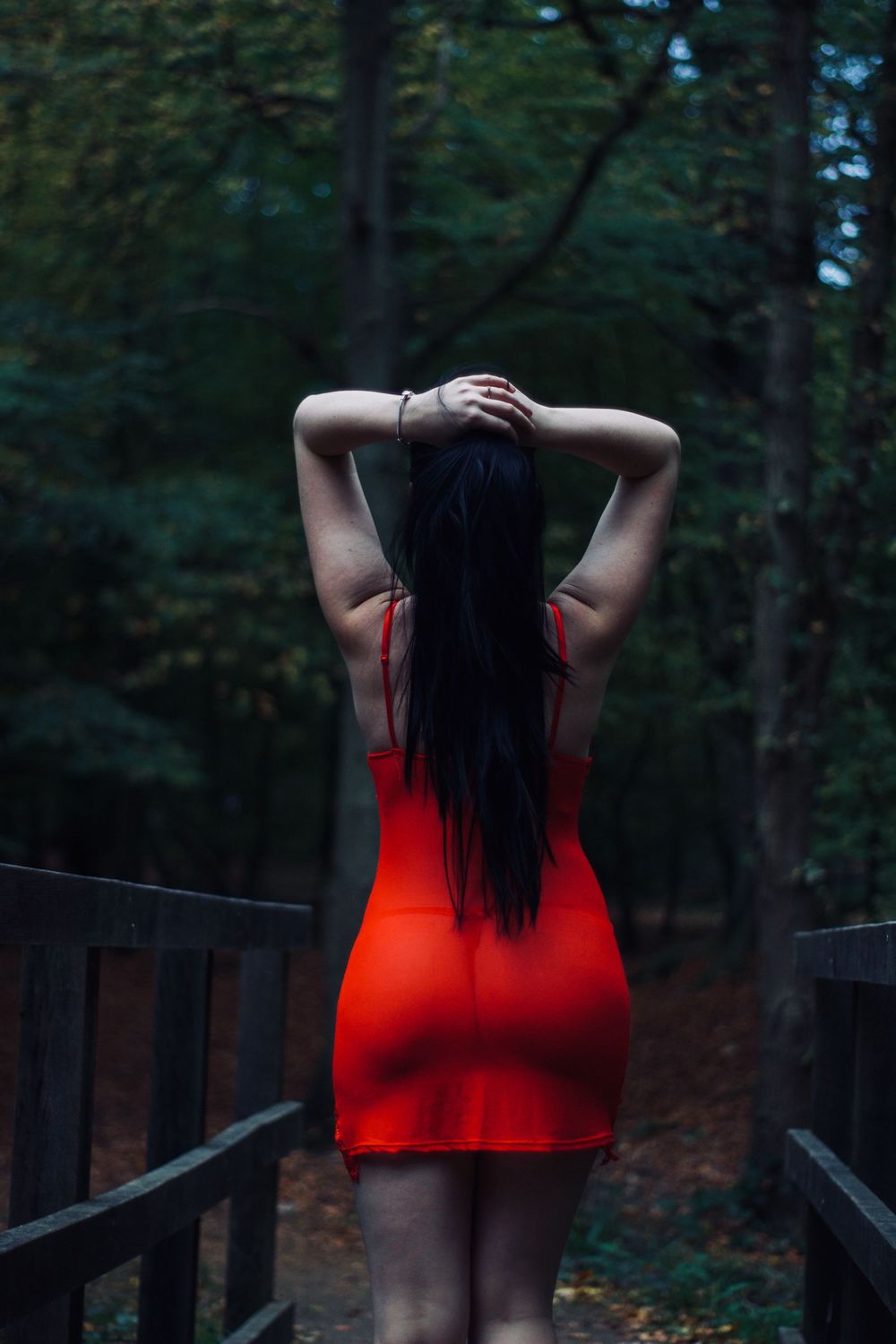 Woman in red dress standing on wooden bridge path in forest.
