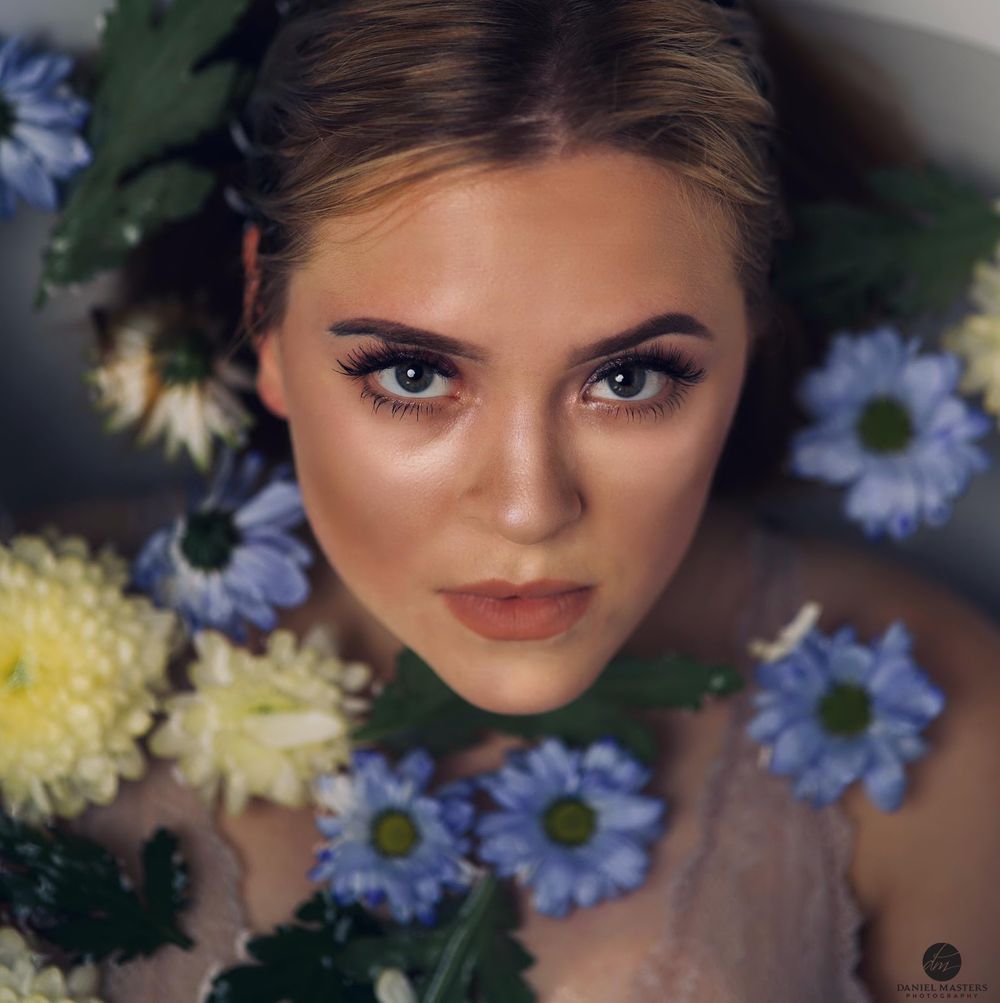 Beauty portrait surrounded by blue and yellow flowers with soft lighting.