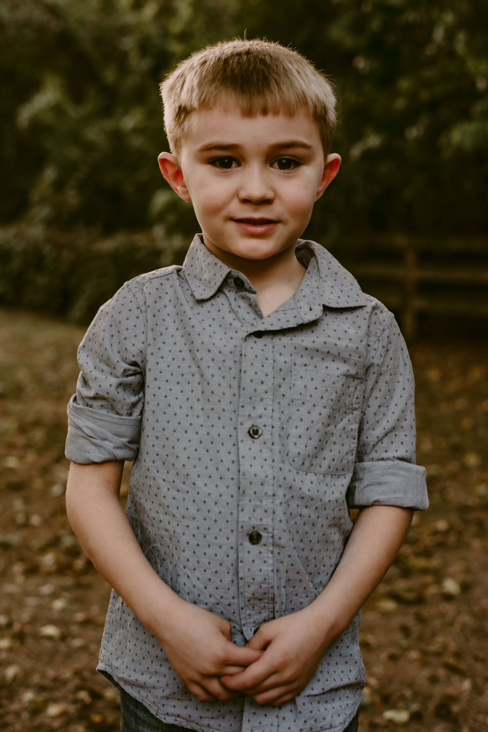 A young child wearing a grey polka dot button-down shirt stands outdoors on a fall day.