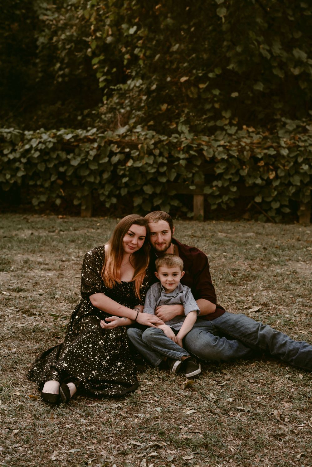 A family lounges together on fallen autumn leaves against a backdrop of ivy-covered walls.