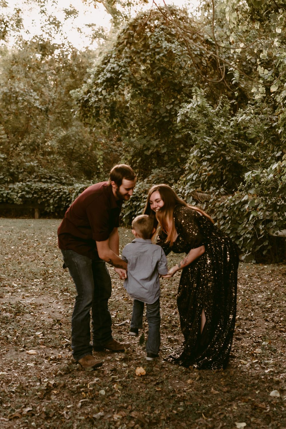 A family shares a playful moment together on fallen leaves in a park setting.