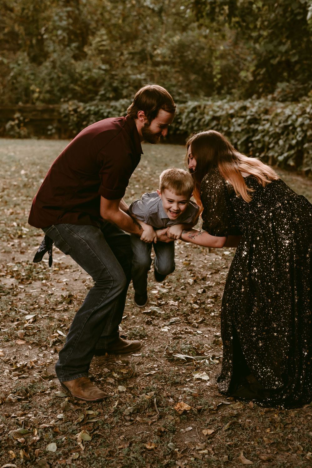 Parents playfully lift and swing their child during an outdoor autumn photoshoot.