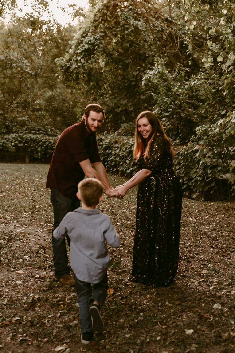 A family plays together in a wooded outdoor setting on fallen autumn leaves.