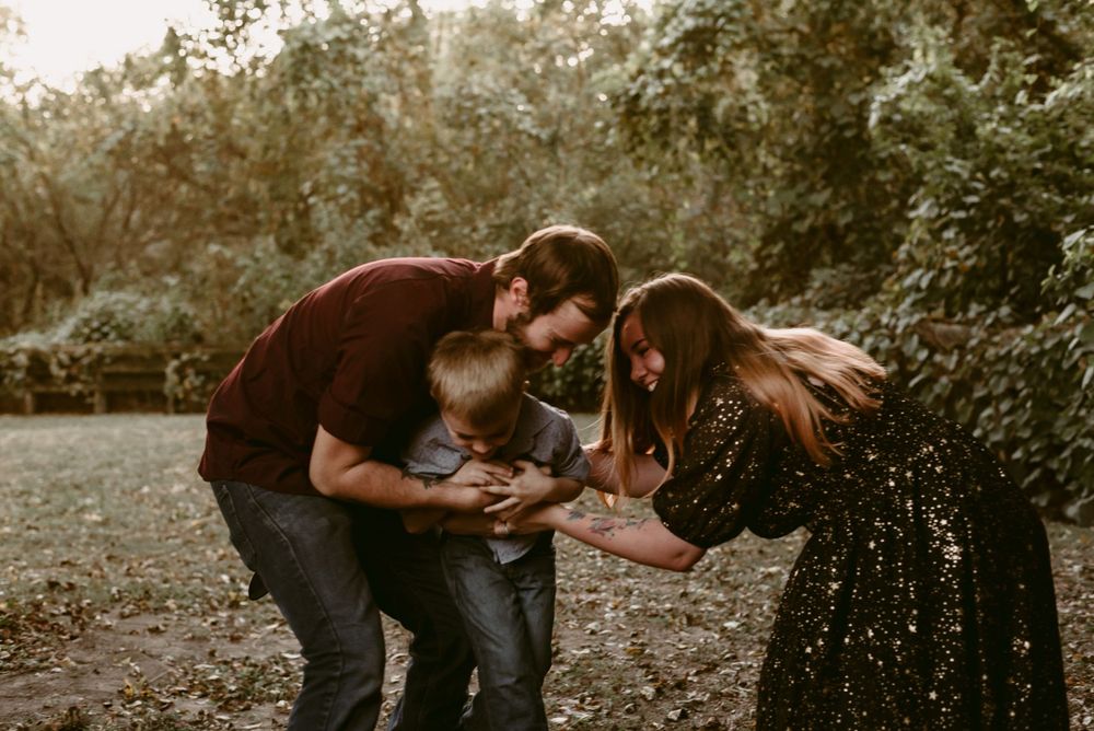 Parents bend down to play with their child during an outdoor photo session.