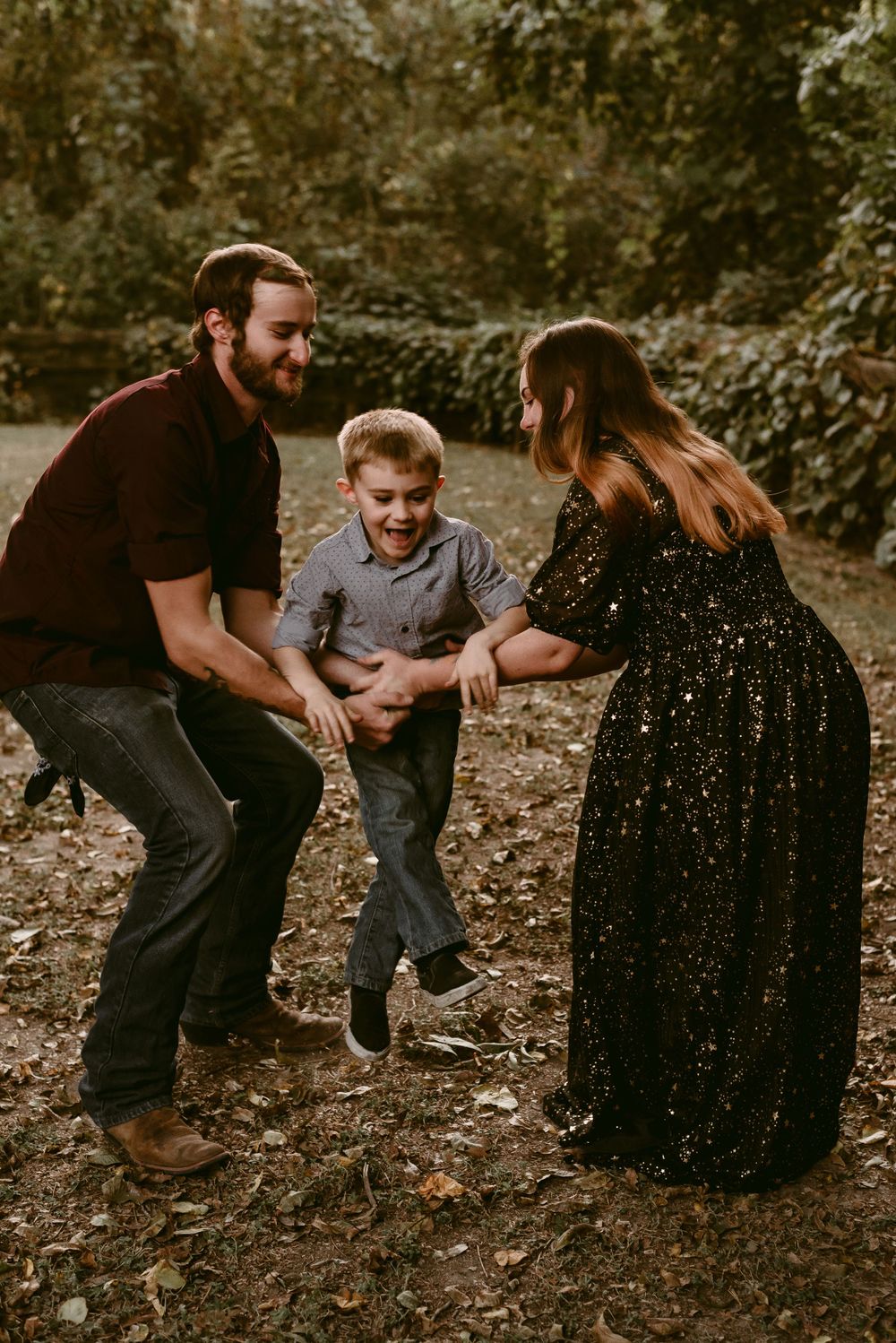 A family plays together outdoors, swinging and laughing among fallen autumn leaves.