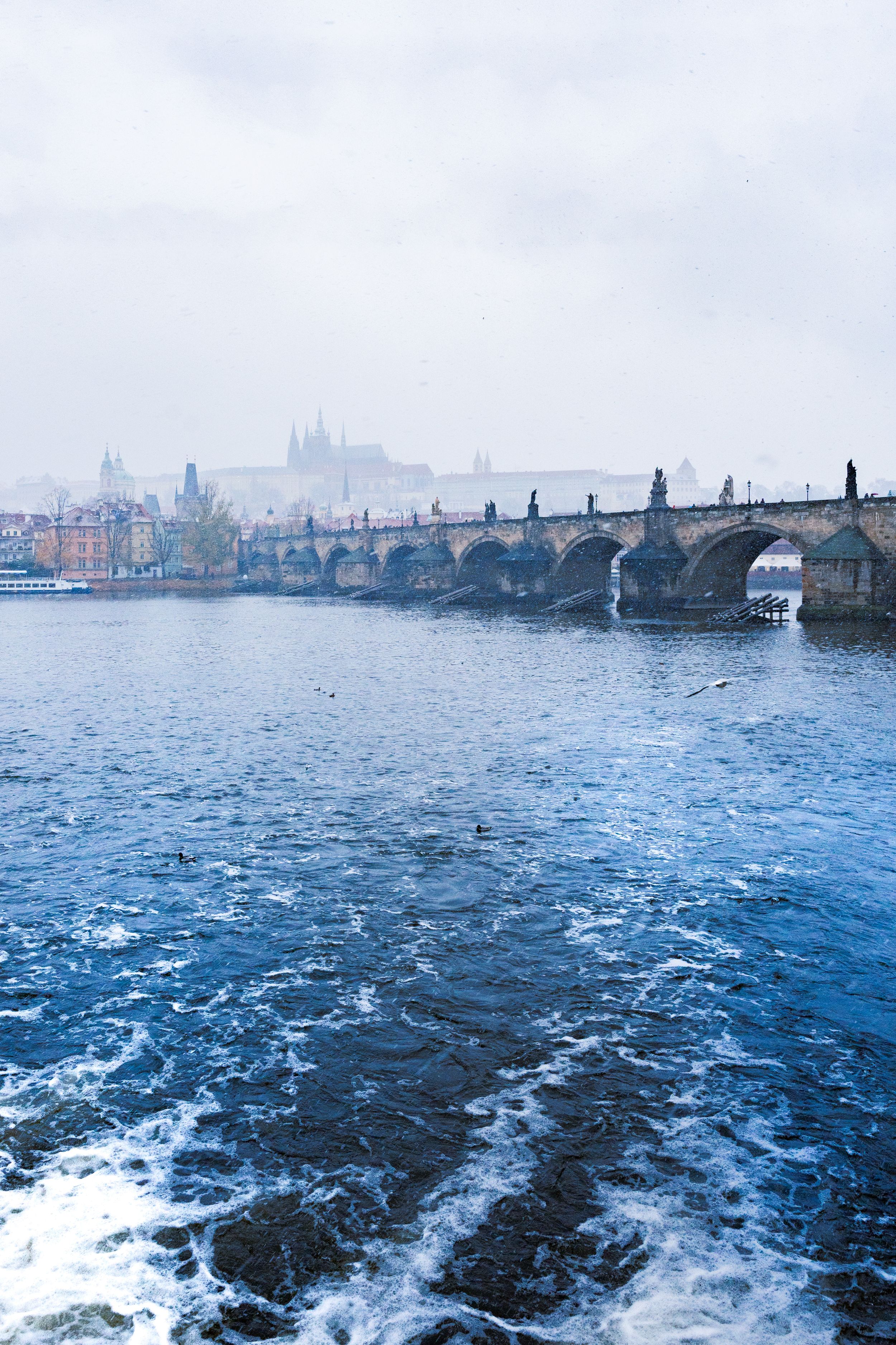 Prague Castle in Prague, Czech Republic on a winter day with snow and rushing water with the Charles Bridge
