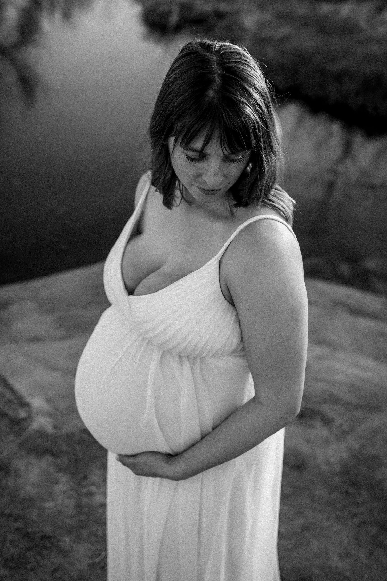 black and white image of a pregnant woman in long white dress, she is looking down over her left shoulder