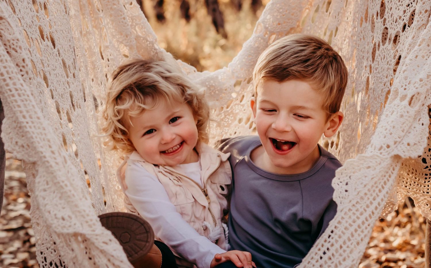 Two children sharing joyful laughter while relaxing in a hammock outdoors.