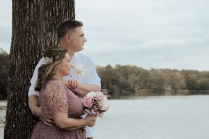 A couple poses together by a tree overlooking a serene lake.