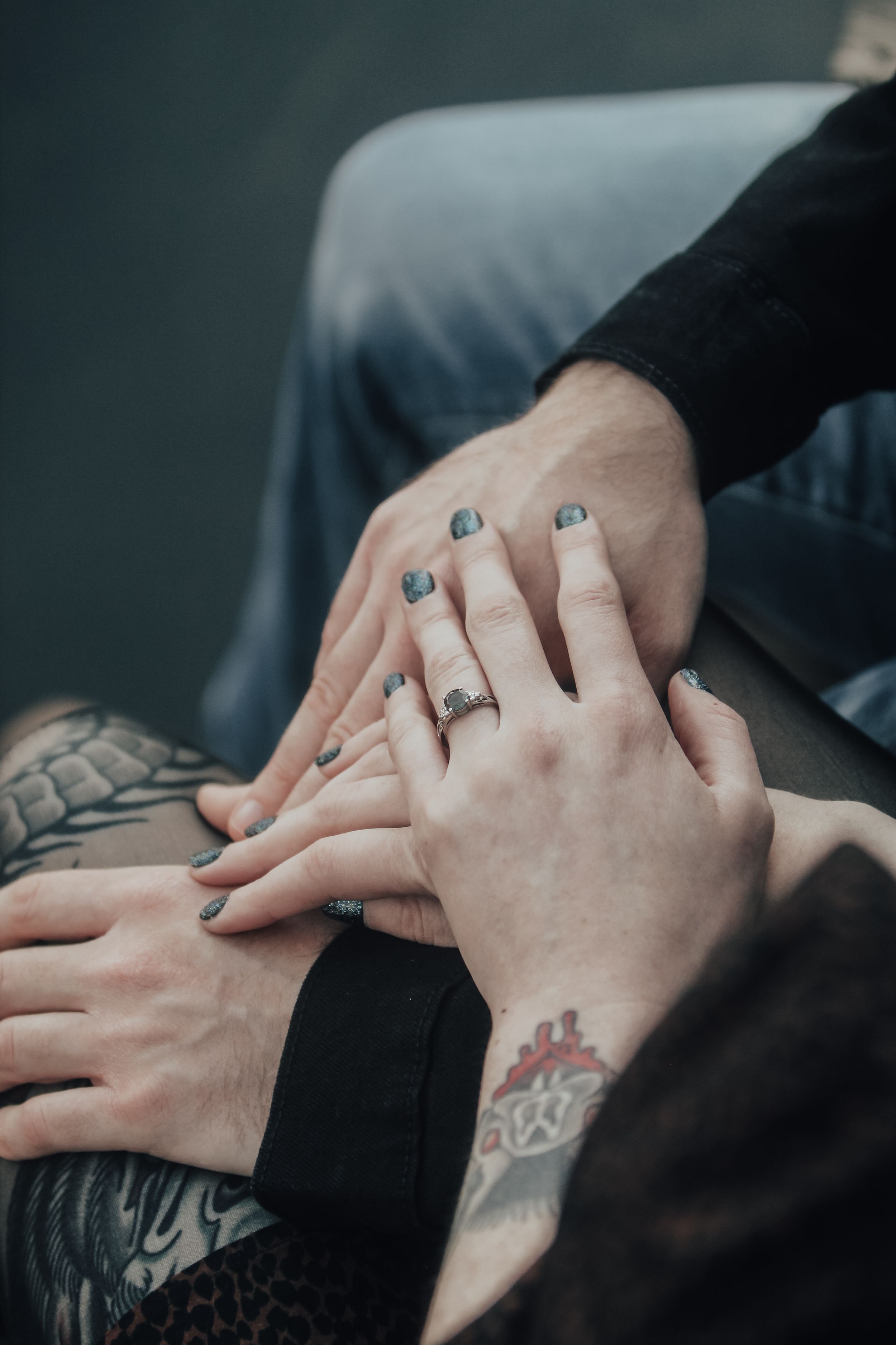 Detailed view of hands with tattoos and rings in gentle embrace.