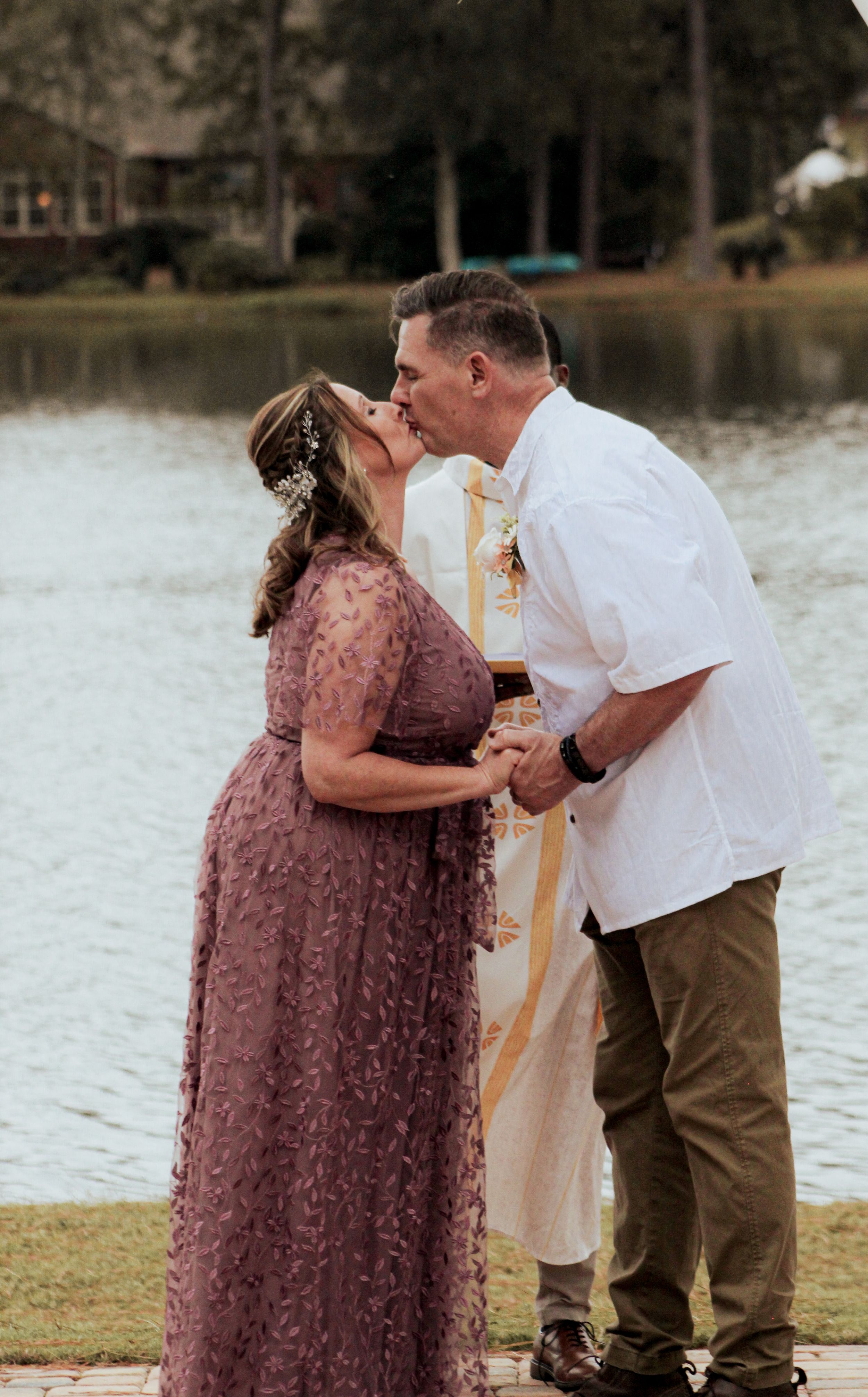 A couple shares a romantic kiss by a lake during their wedding ceremony.