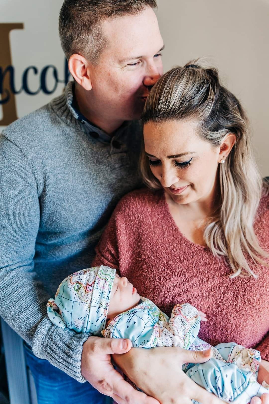 Parents share intimate moment while holding newborn wrapped in floral swaddle.