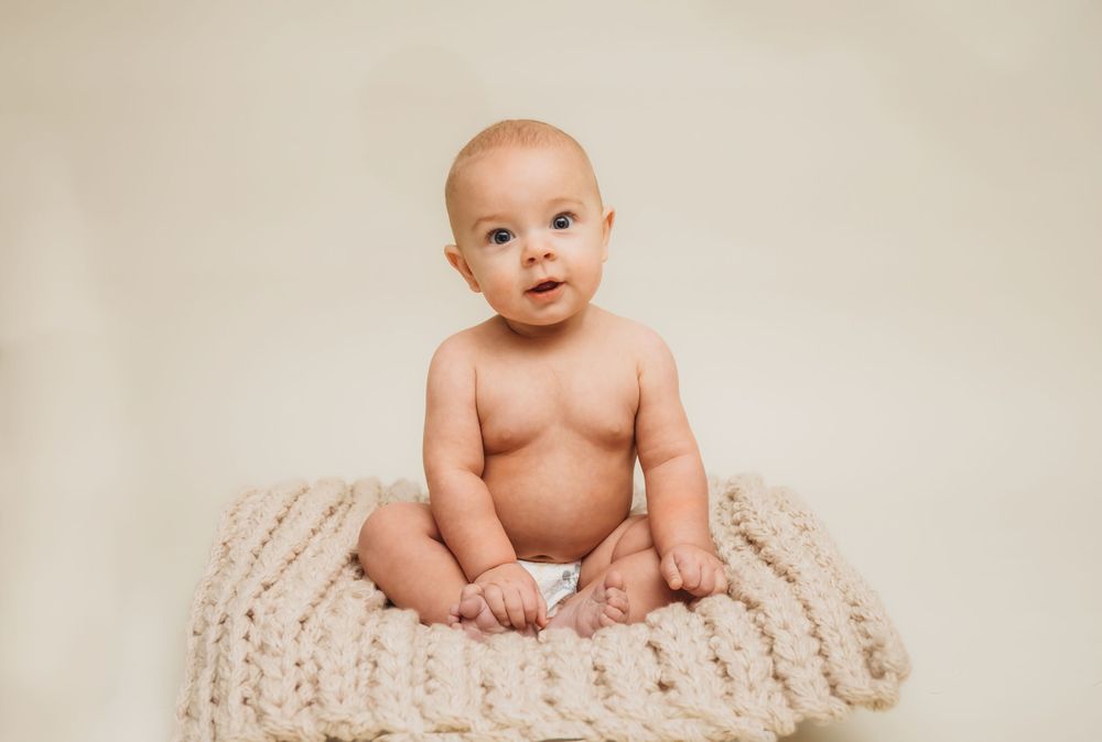 Baby sitting on cream knitted blanket during studio photoshoot.