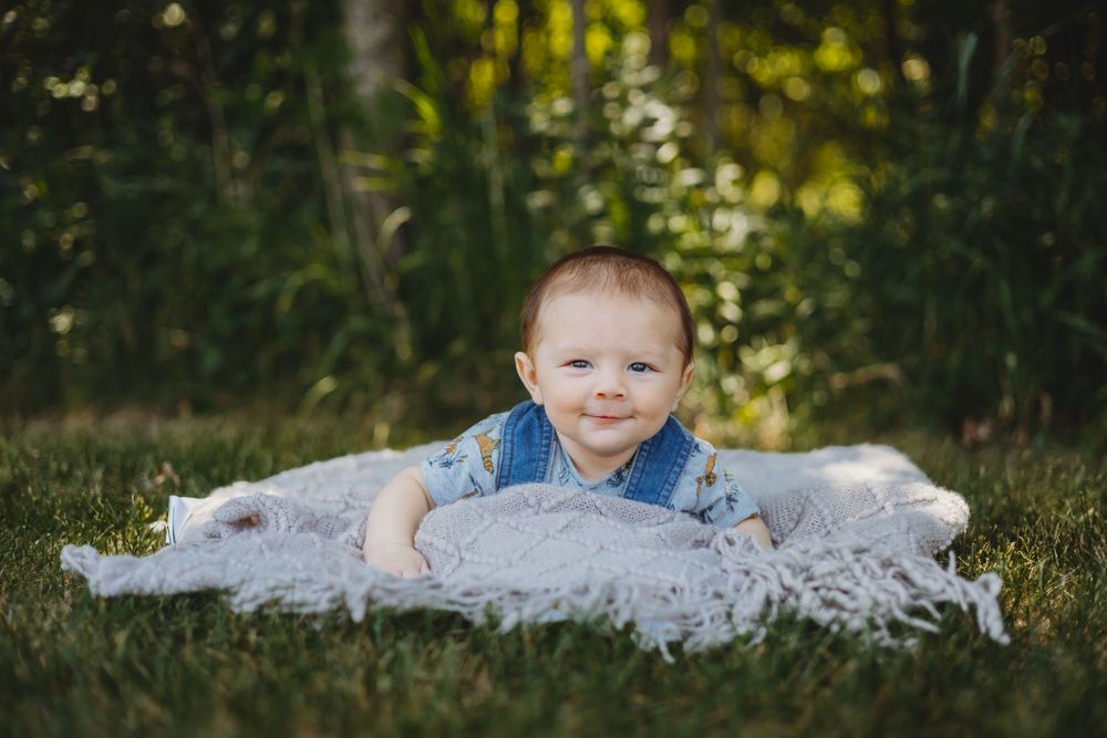 Child poses on white blanket in outdoor garden setting with bokeh background.