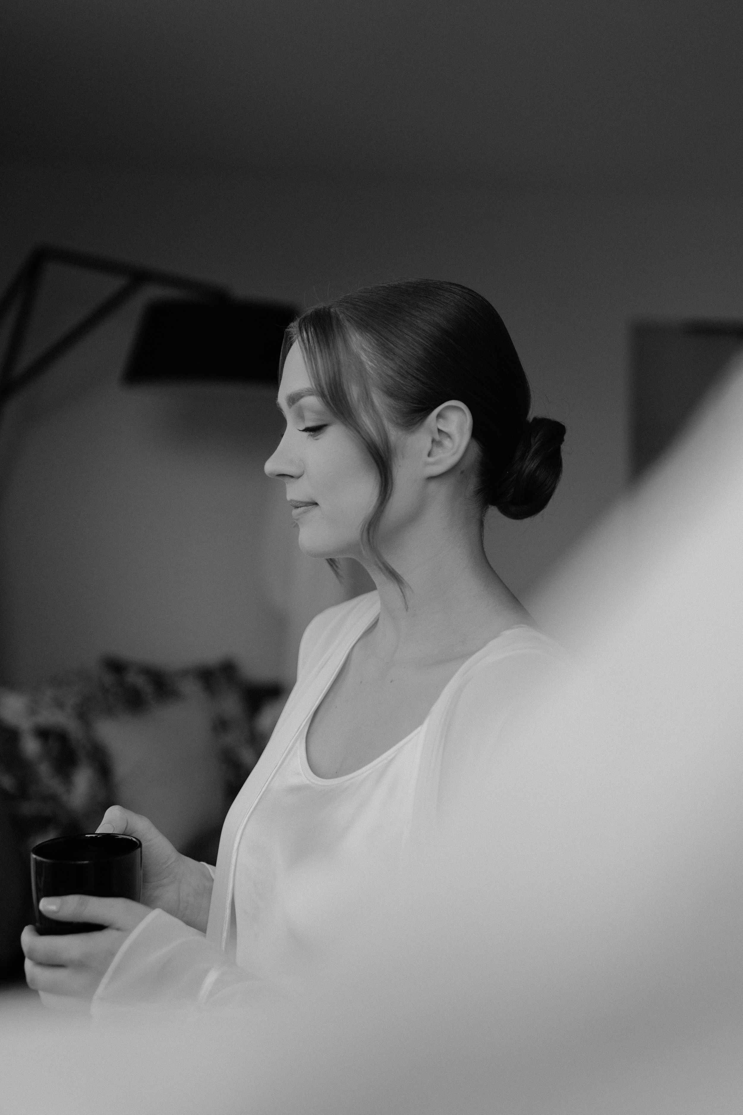 Black and white portrait of person in white robe holding coffee cup during wedding preparations.