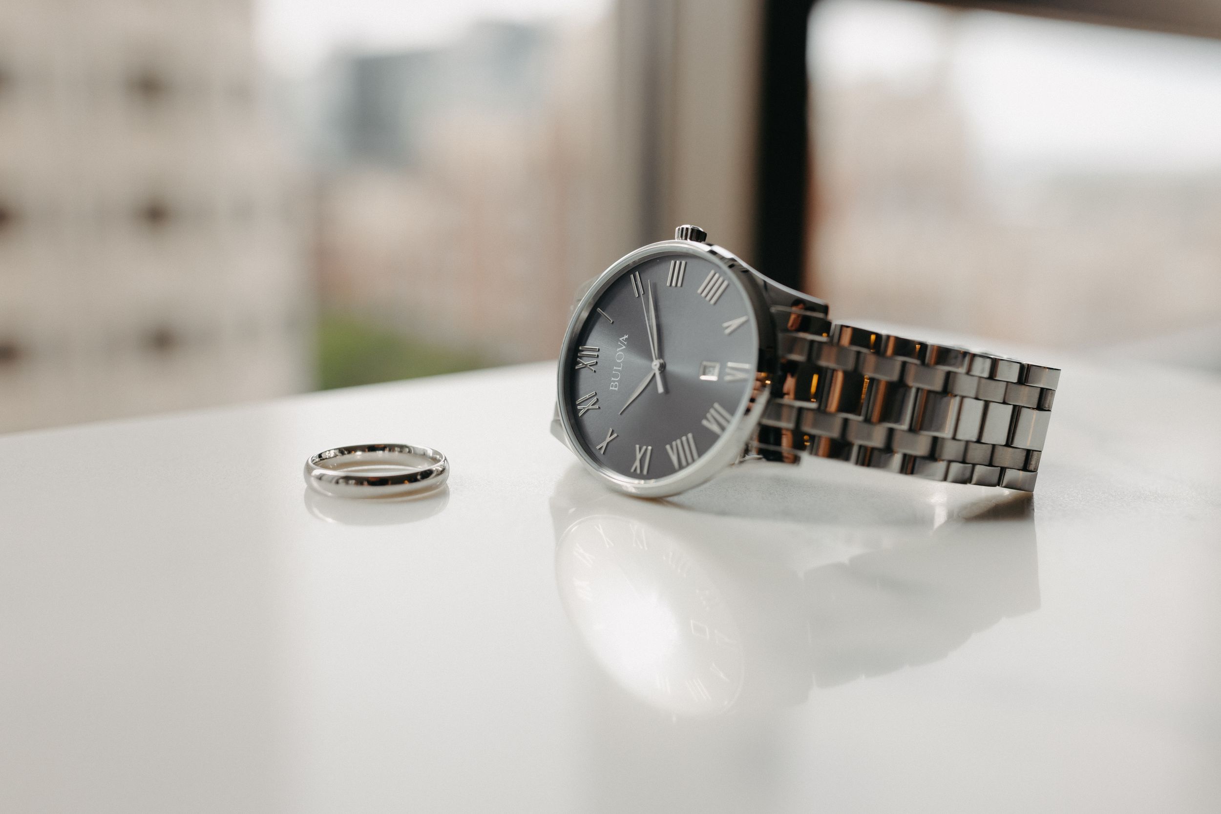 Silver watch and wedding ring displayed on white surface.