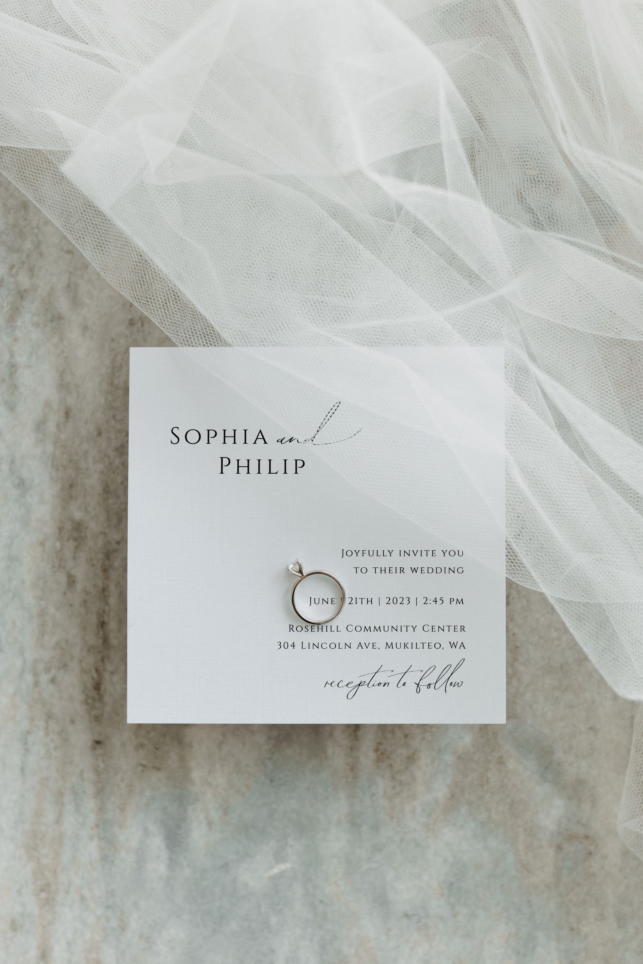 Elegant wedding invitation with rings displayed on white tulle fabric.