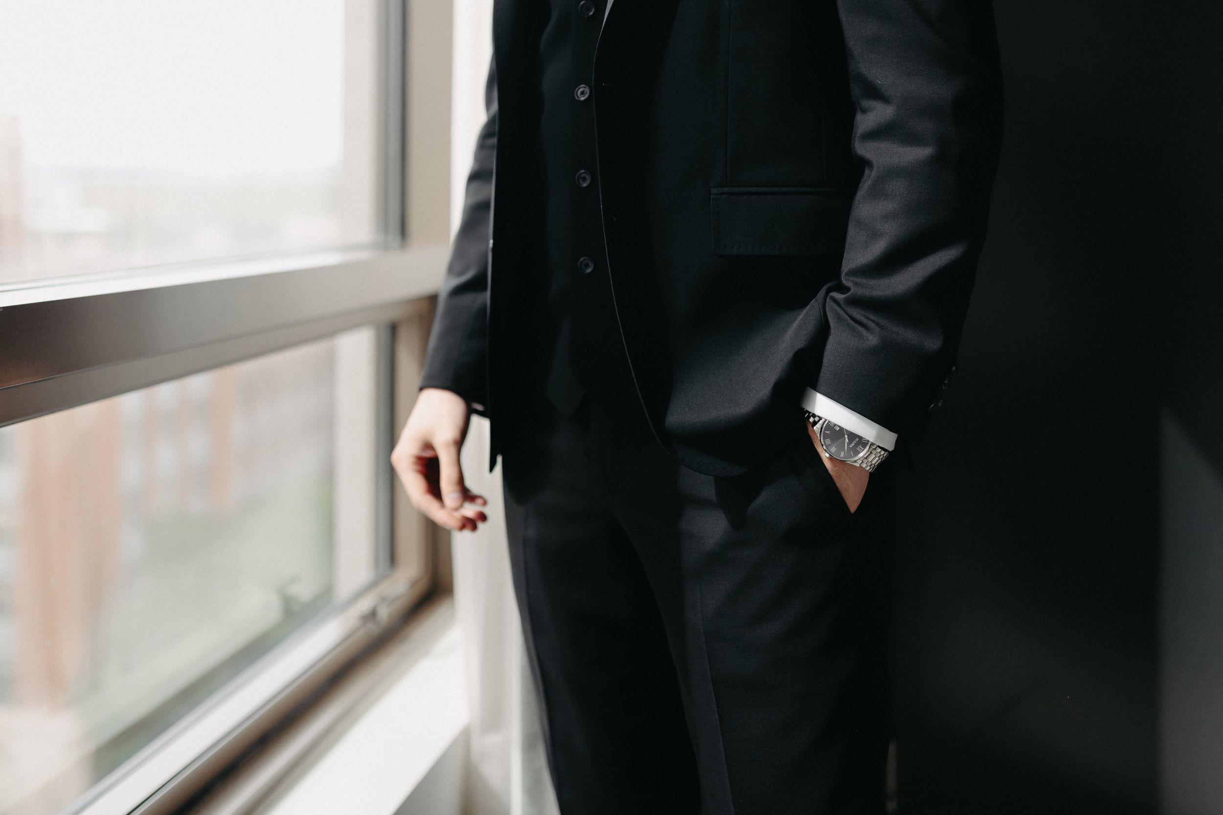 Detail shot of black tuxedo sleeve and pocket against window light.