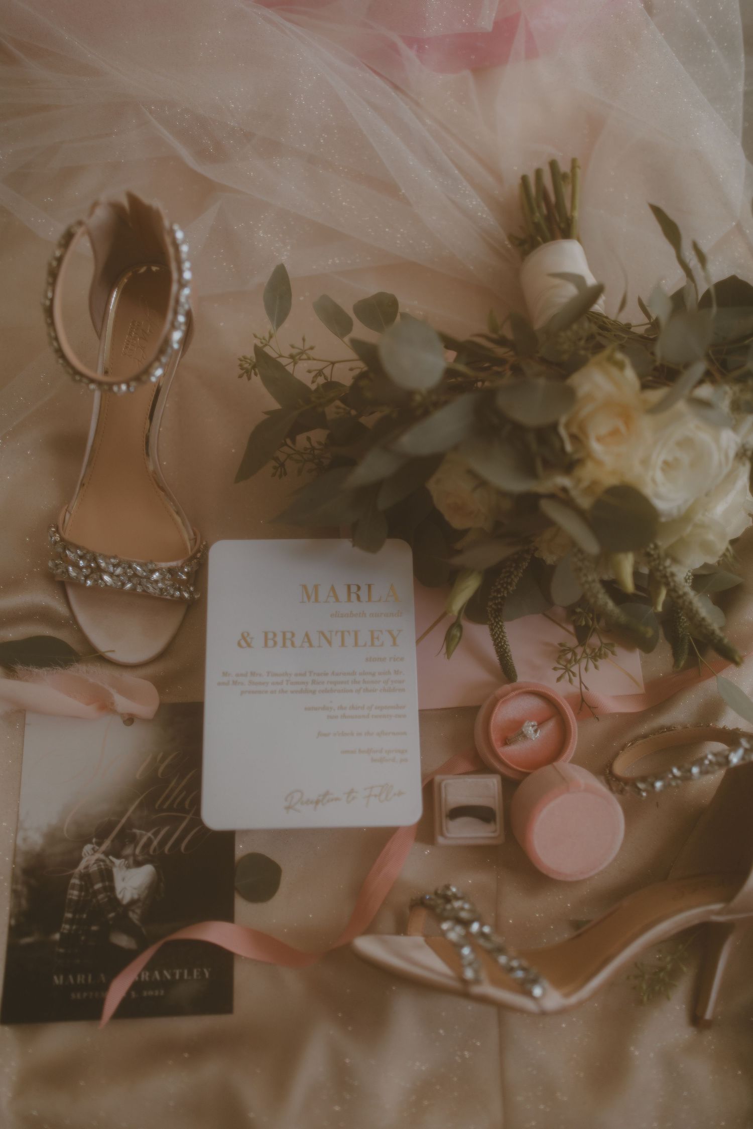 Wedding details flatlay with invitation, shoes, flowers and rings in soft pink tones.