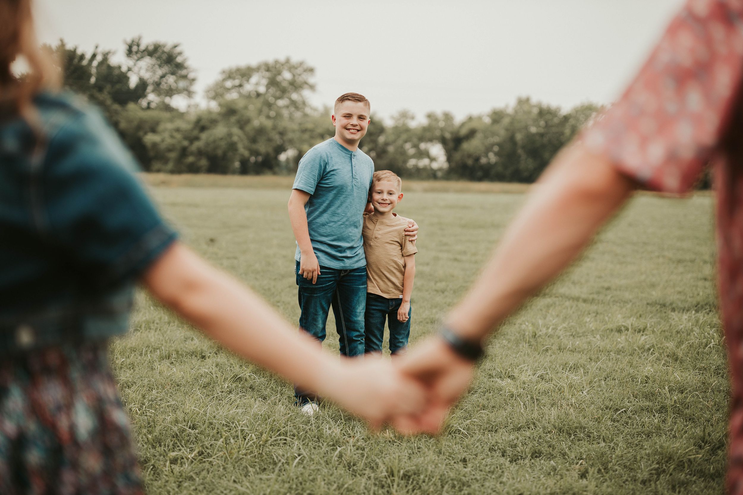 Family holding hands in a green field during golden hour.