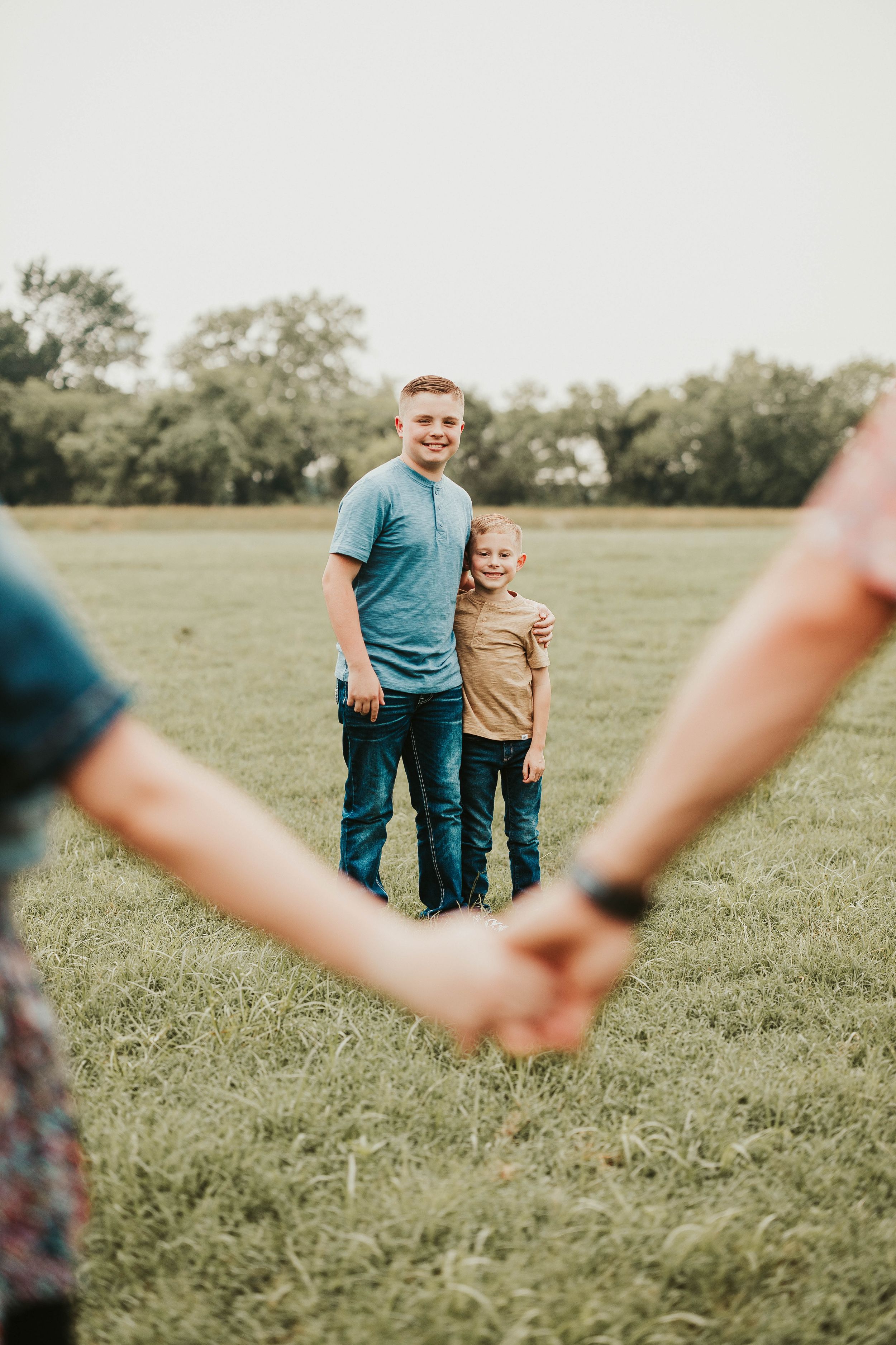 Family members standing together in a sunny meadow with blurred foreground elements.