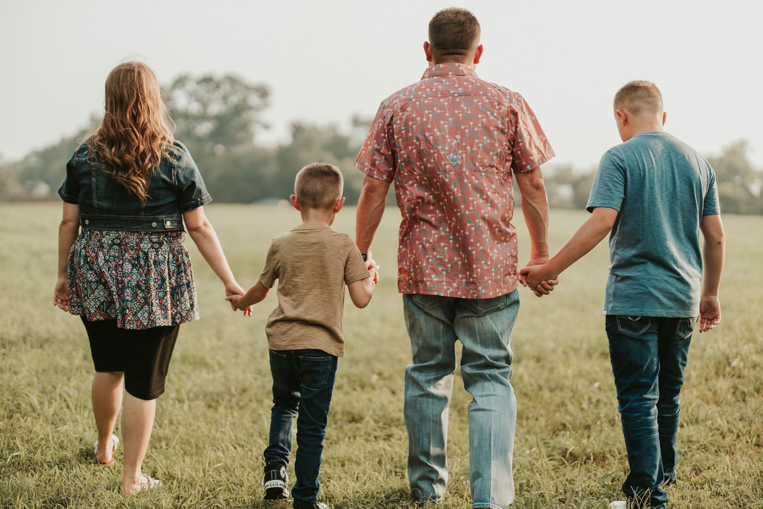 Family walking together holding hands in a grassy field at sunset.