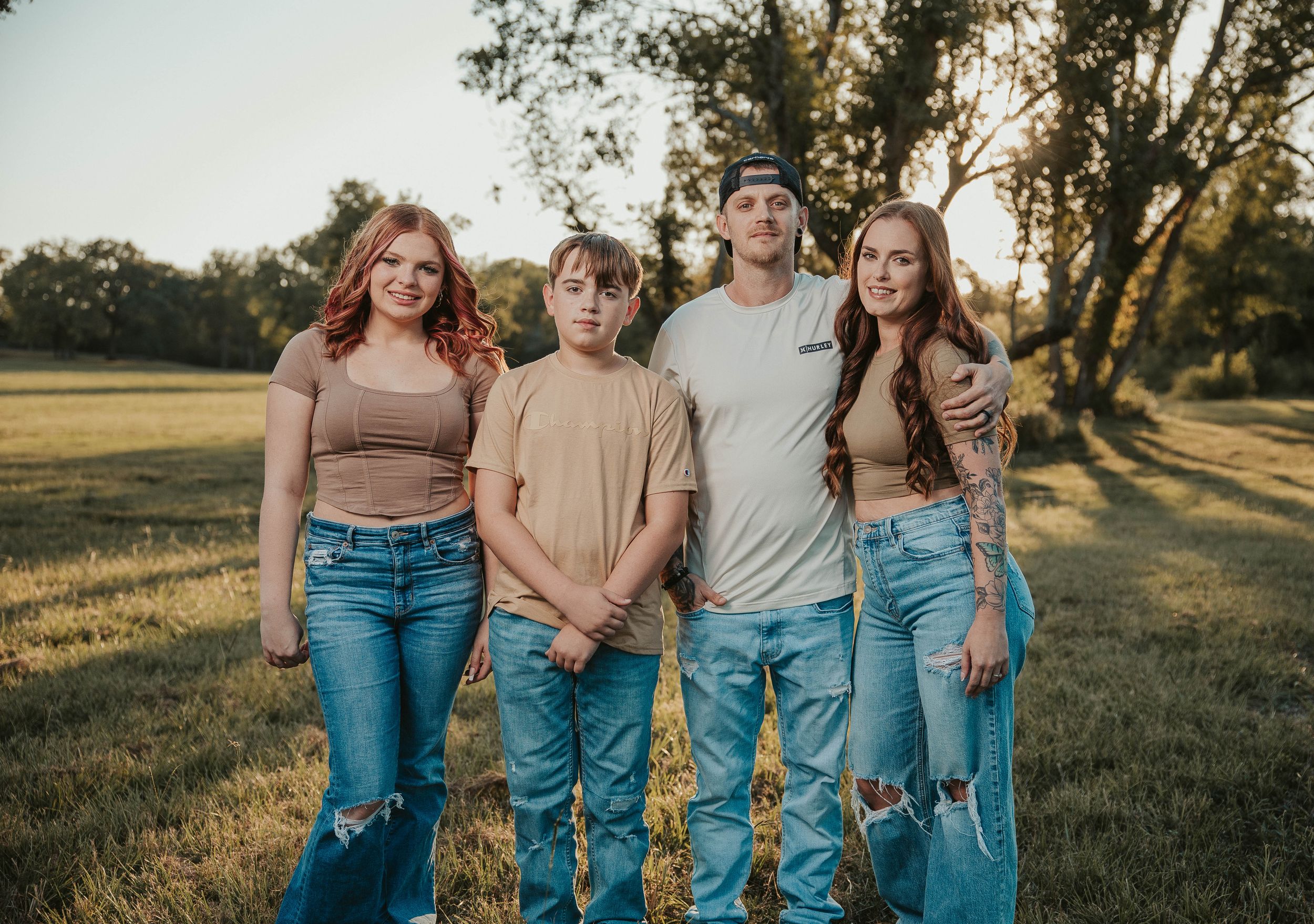 Group of friends in casual denim outfits posing together in a golden sunlit field at sunset.