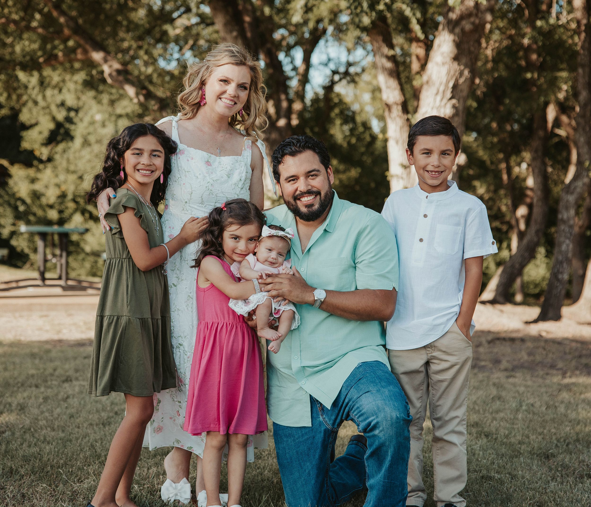 A cheerful family group photo taken outdoors with everyone dressed in coordinating casual outfits.