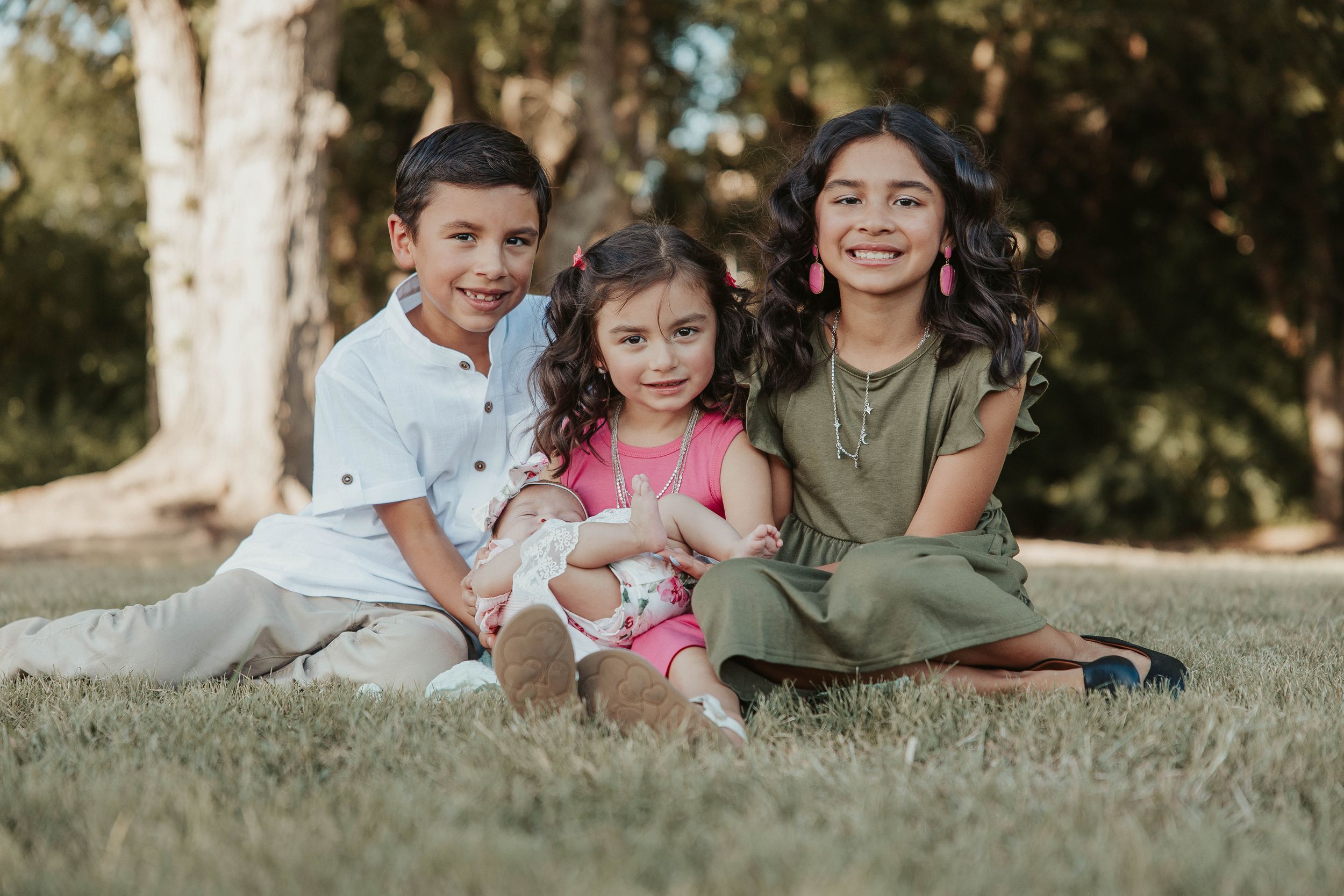 Three siblings sit together on grass during an outdoor family photoshoot.