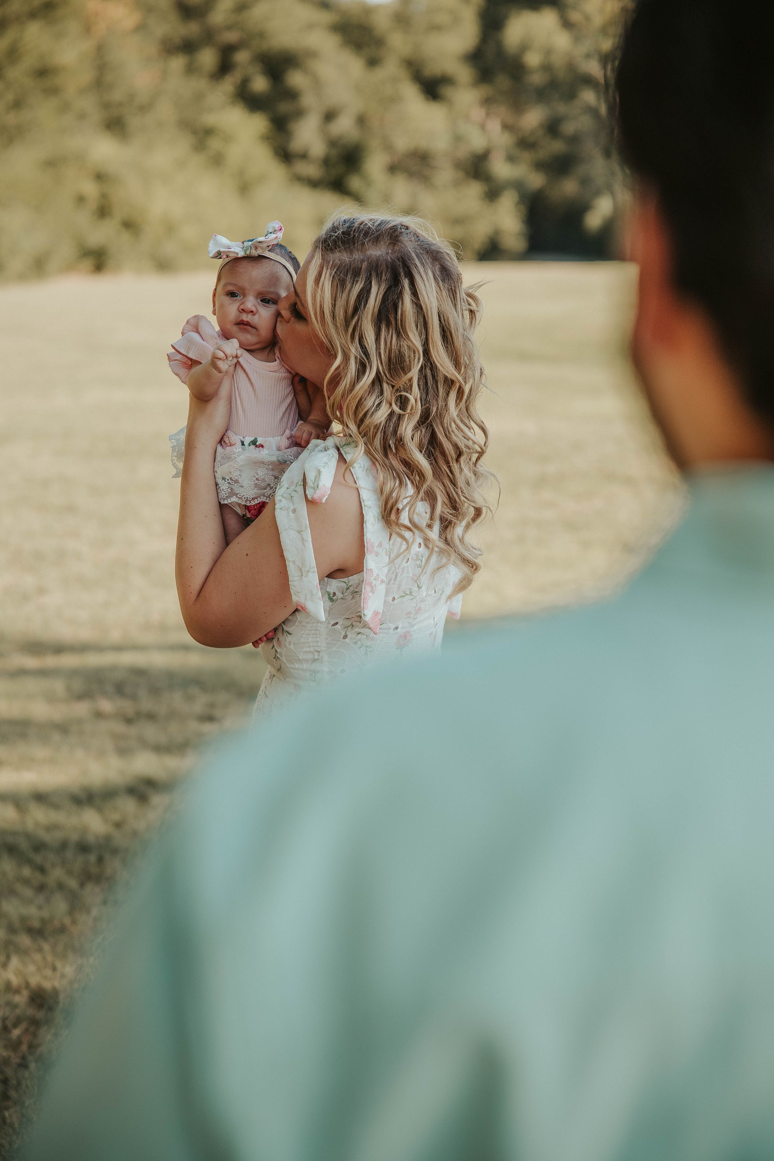A tender moment with a baby being held up against a sunny outdoor background.