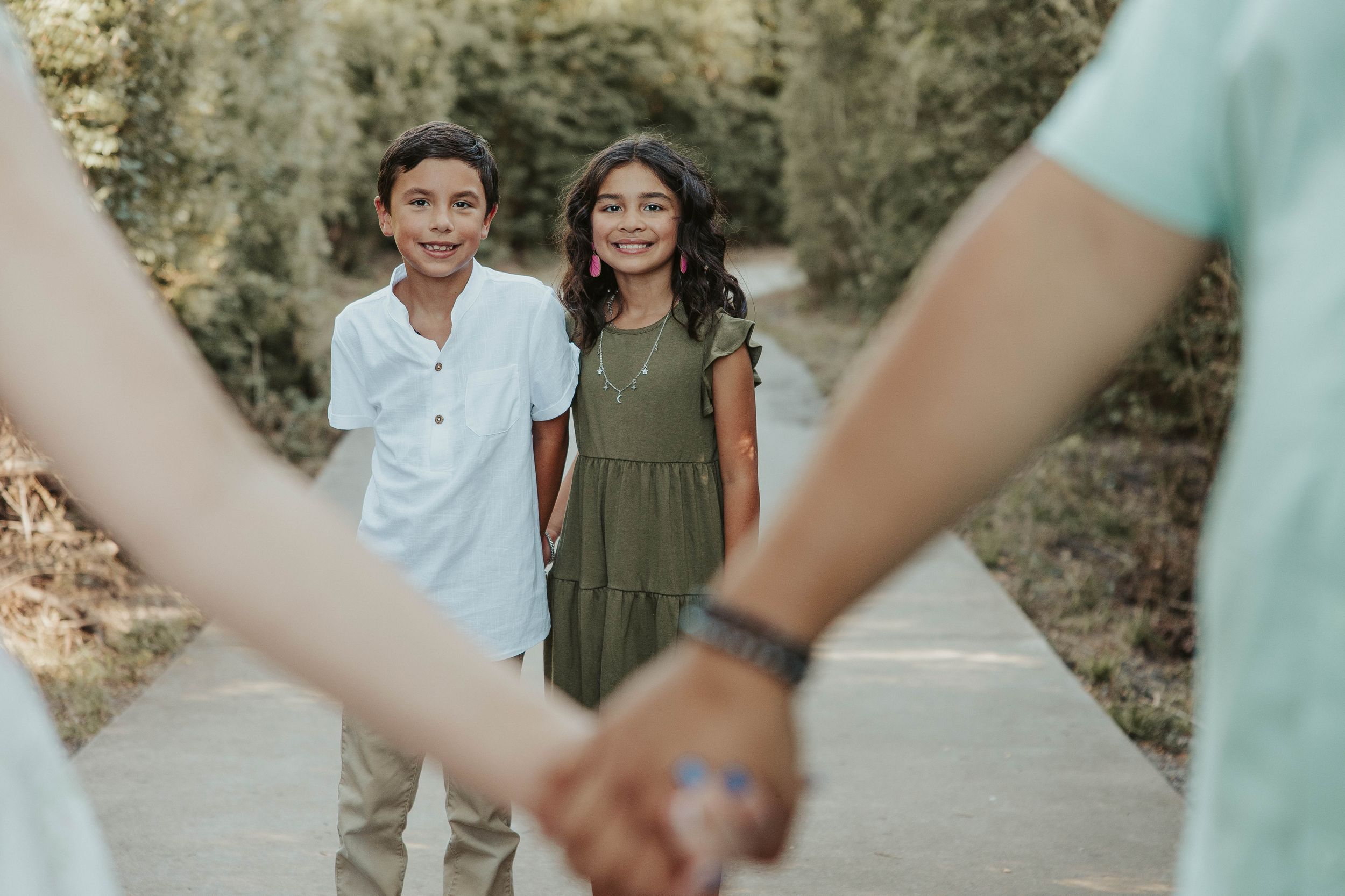 Two children pose on a path while adults hold hands in the foreground of the shot.