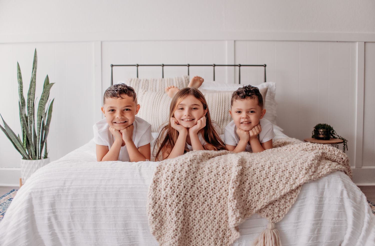 Family having fun hiding under a cozy knit blanket in a bright white bedroom.
