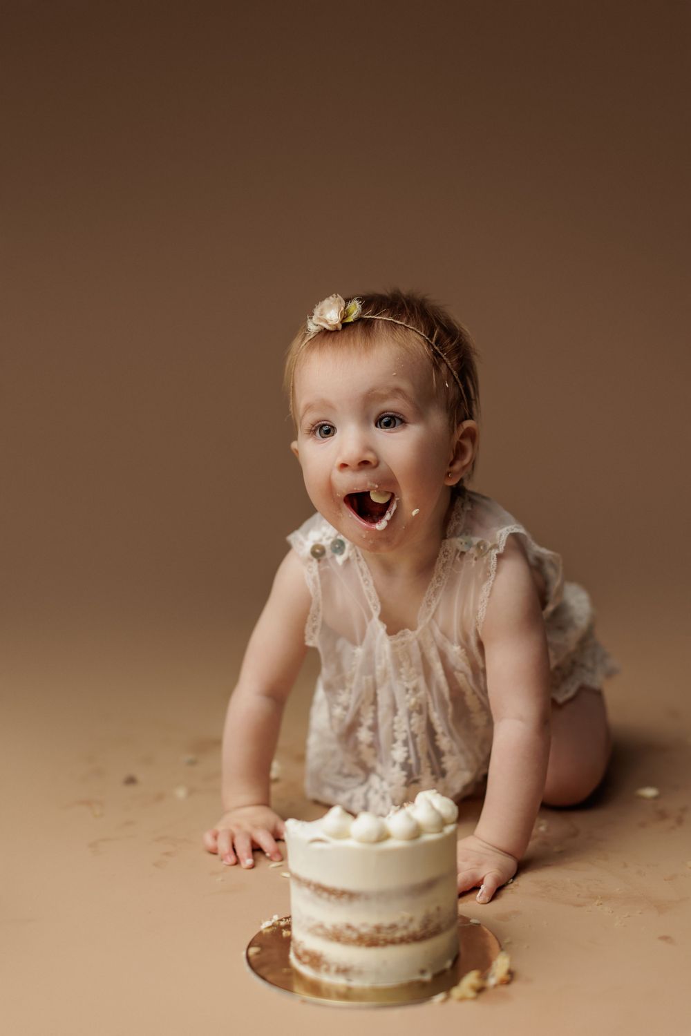 Excited baby reaching for birthday cake during studio cake smash session.