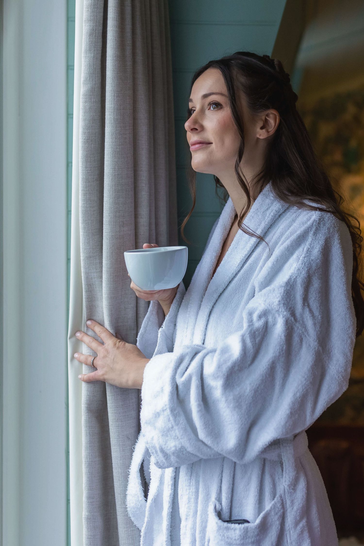East Sussex bride looking out the wedding venue window in her dressing gown with a cup of tea.