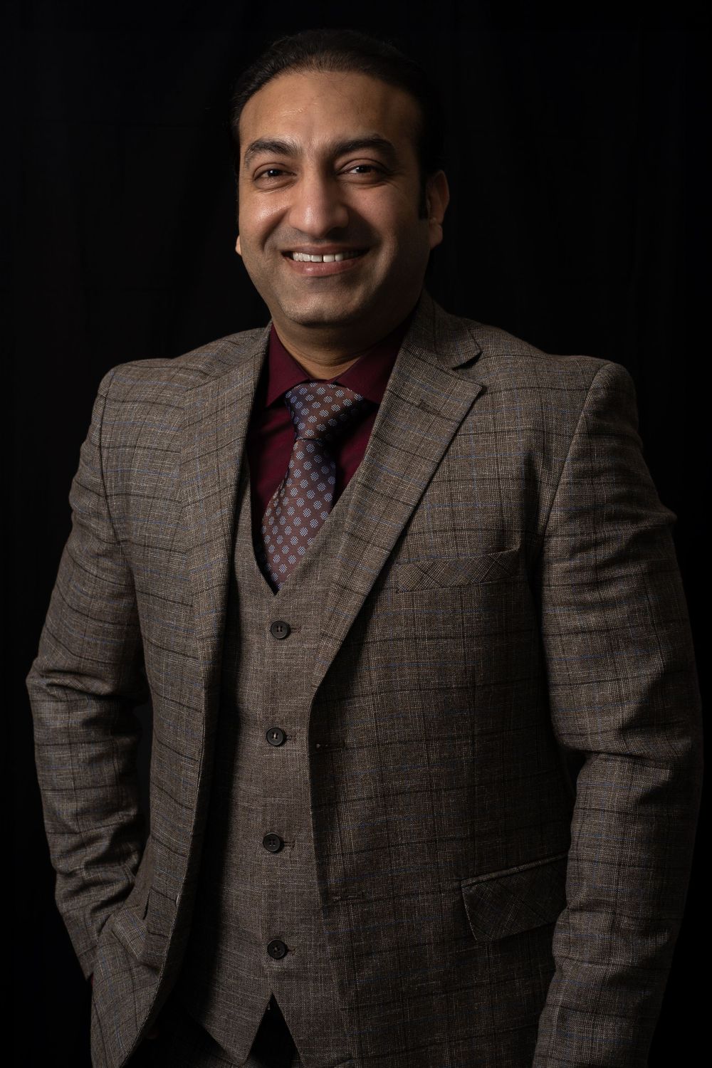 Studio portrait of man in brown plaid three-piece suit against dark background.