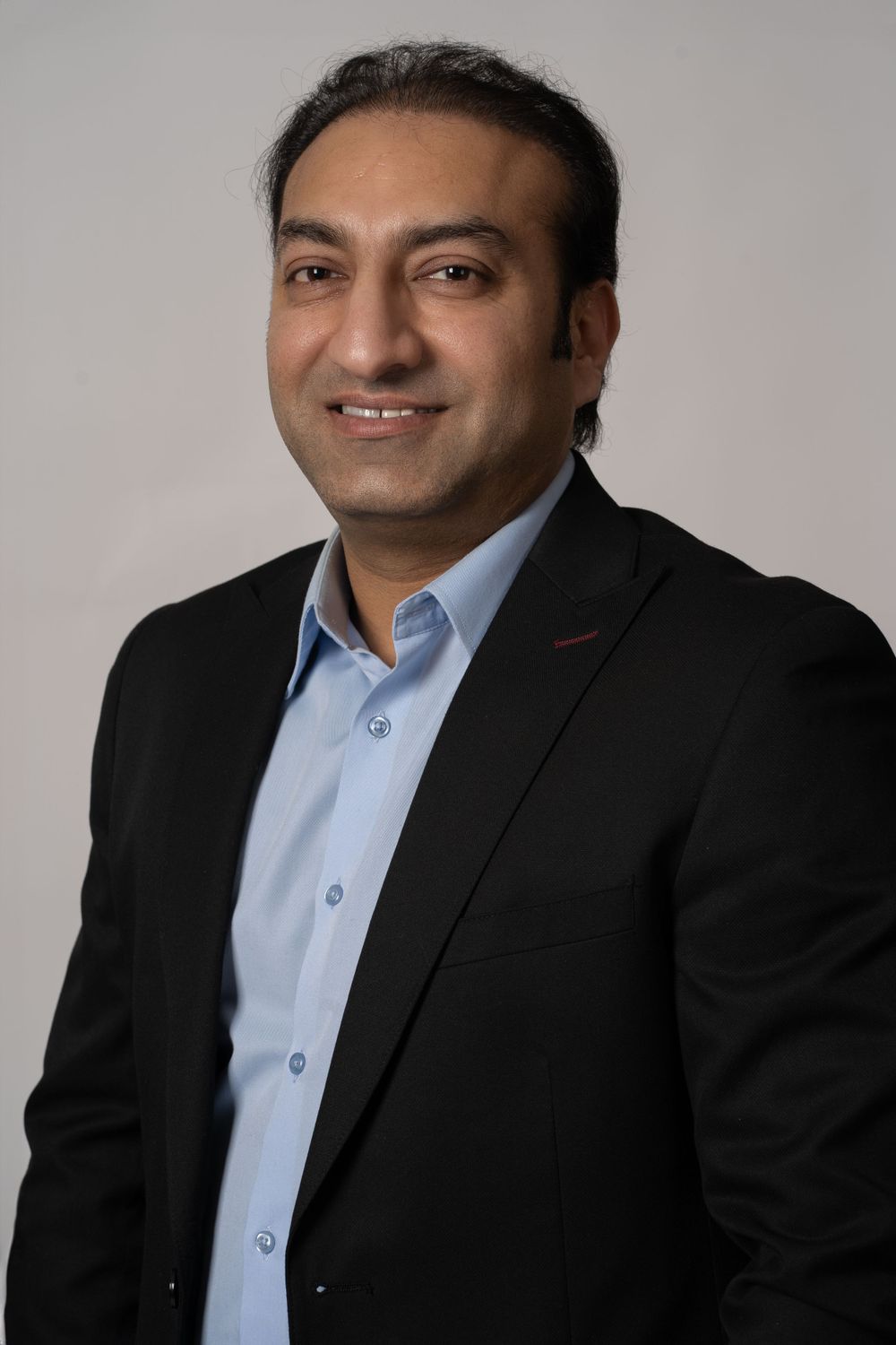 Professional headshot of man in dark suit and light blue shirt.