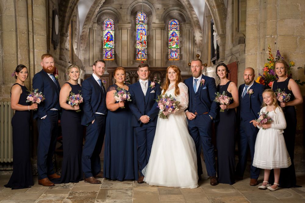 Wedding party in navy and white formal attire posed under church stone archway.