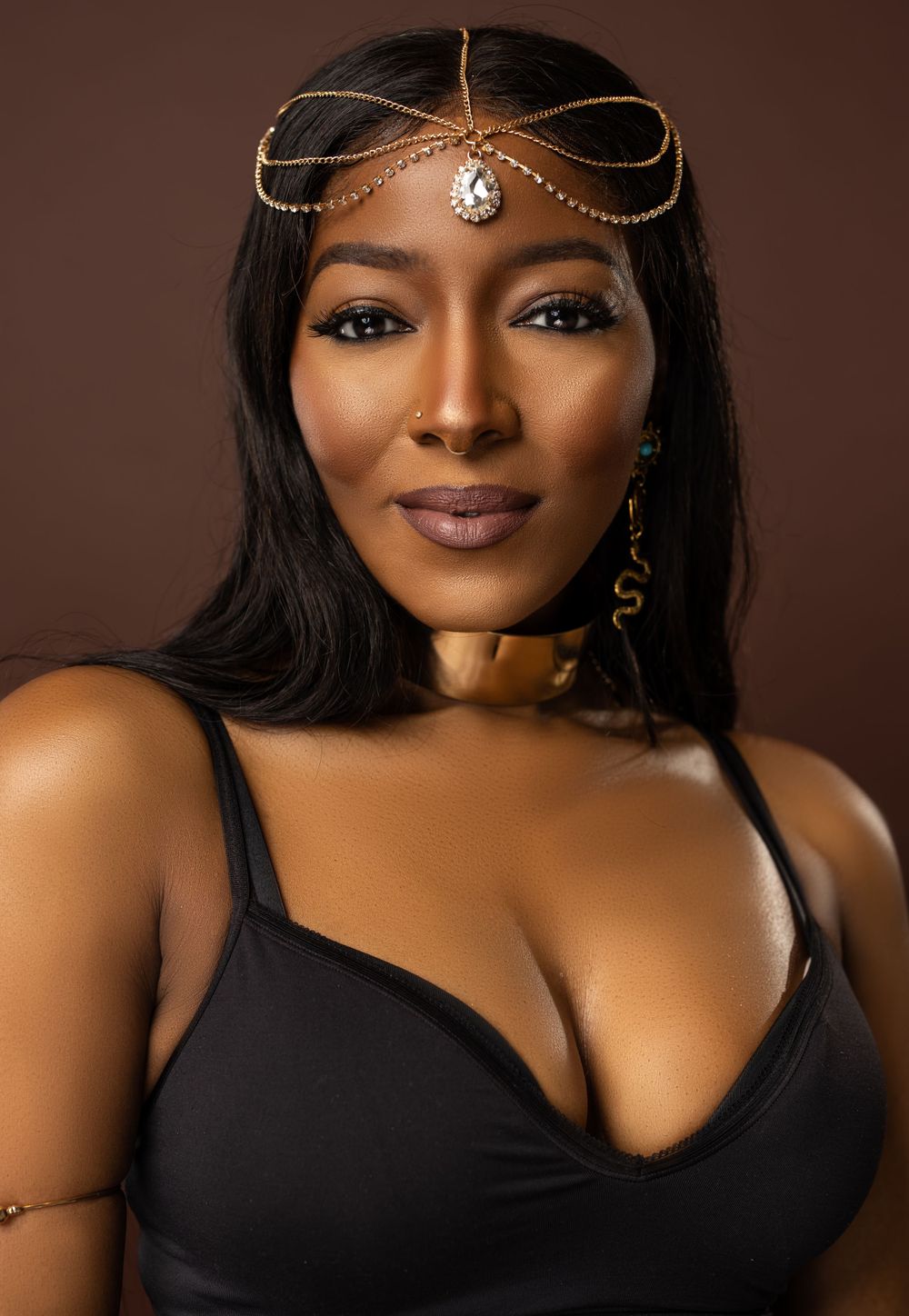 Studio portrait with delicate gold headpiece and black top against dark brown background.