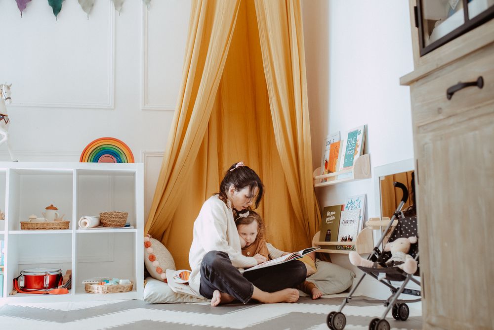 A reading nook with yellow curtains, rainbow decor, and white shelving units.