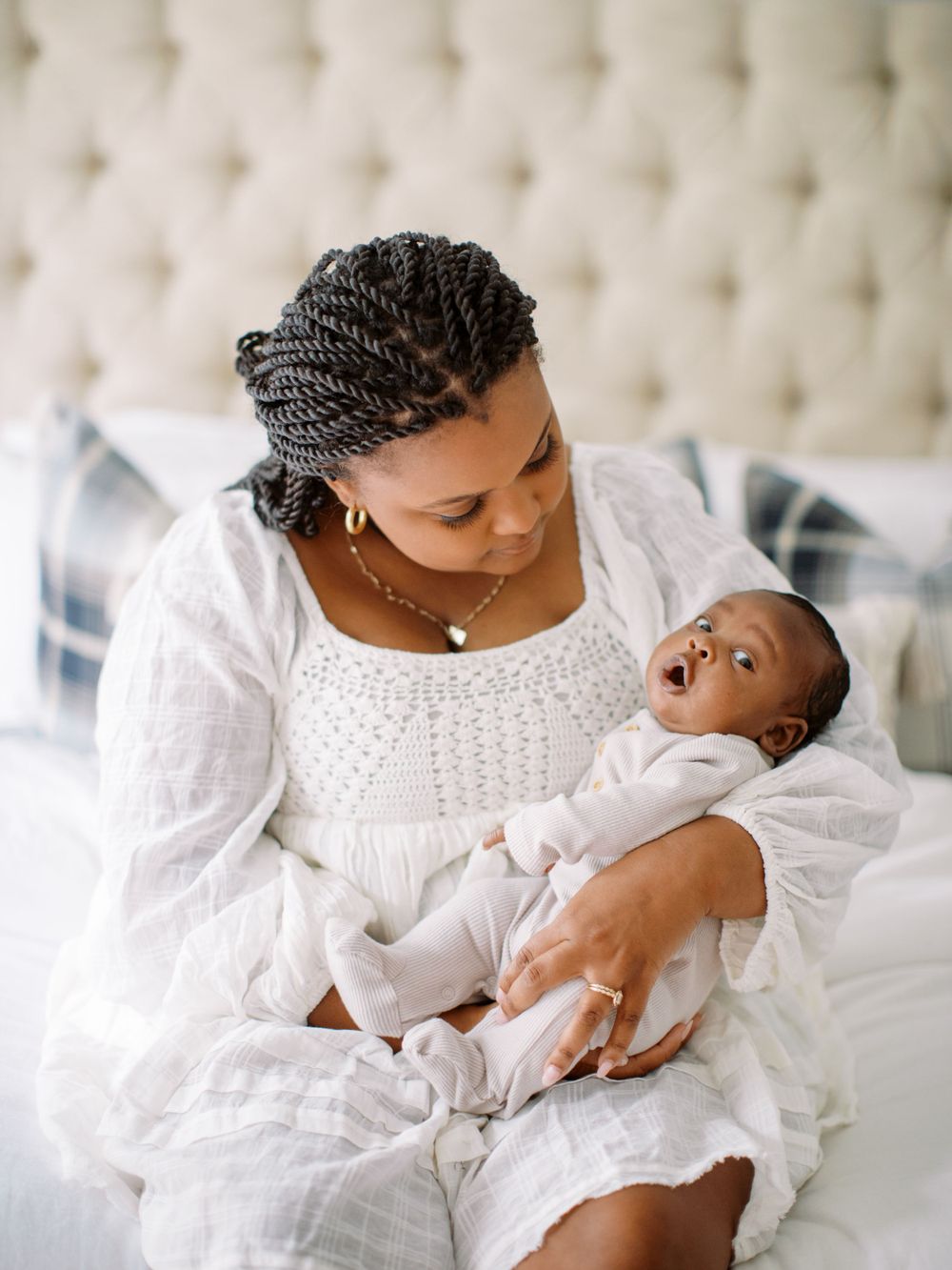 Nurturing moment captured between adult and infant in matching white outfits on a bed.