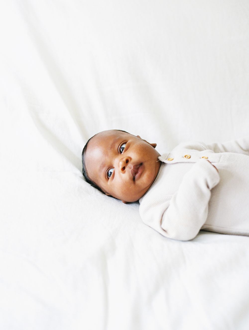 Smiling baby wearing white sleeper on light colored bedding.