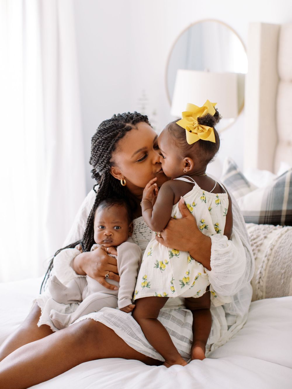 Tender moment in white room showing affectionate embrace between parent and children wearing matching light outfits.