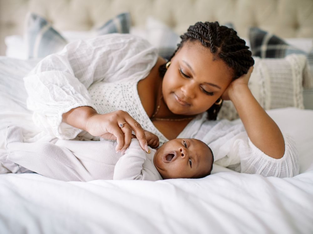 Sweet bonding moment between adult and infant relaxing together on white bedsheets.